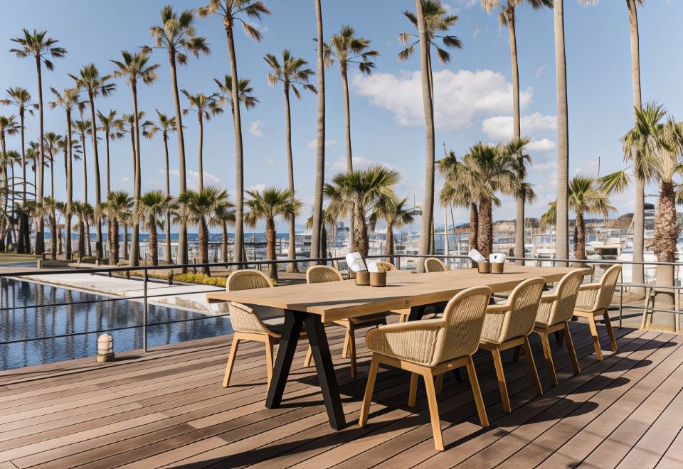 a wooden dining table with chairs is set up on a deck overlooking palm trees and a pool at Malibu Hotel