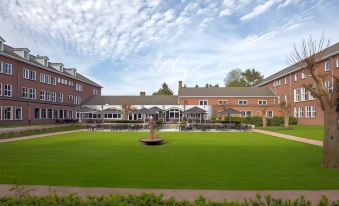 a large brick building with multiple buildings and a well - maintained lawn area in front of it at Fletcher Kloosterhotel Willibrordhaeghe