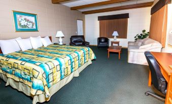a hotel room with a bed , couch , and chairs , all arranged in a spacious and well - lit setting at Wrangler Inn Mobridge