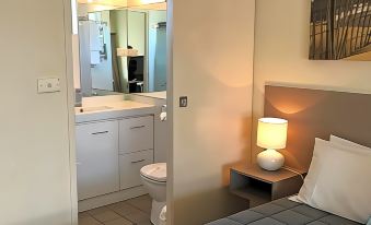 a bedroom with a bed , nightstand , and lamp is shown with an open door leading to a bathroom at Robetown Motor Inn & Apartments