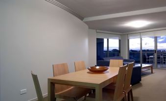 a dining room with a wooden table , chairs , and a bowl on the table , surrounded by a living area with a couch and windows at Scarborough Beach Resort