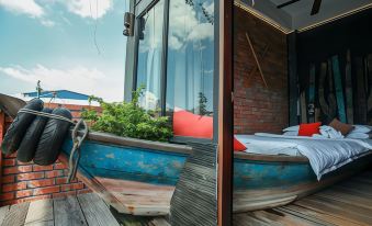 a wooden deck with a blue boat bed , red cushions , and a potted plant , overlooking a red brick building at The Happy 8 Retreat @ Kuala Sepetang