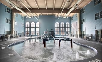 an indoor swimming pool with a large circular fountain in the center , surrounded by wooden floors and white columns at Hilton Garden Inn Oconomowoc