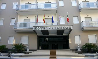 "a modern building with multiple flags and the name "" hotel luxon "" written in white letters" at Hotel Luxor