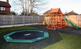 a backyard with a trampoline and a wooden play structure , surrounded by grass and trees at Crossways Inn