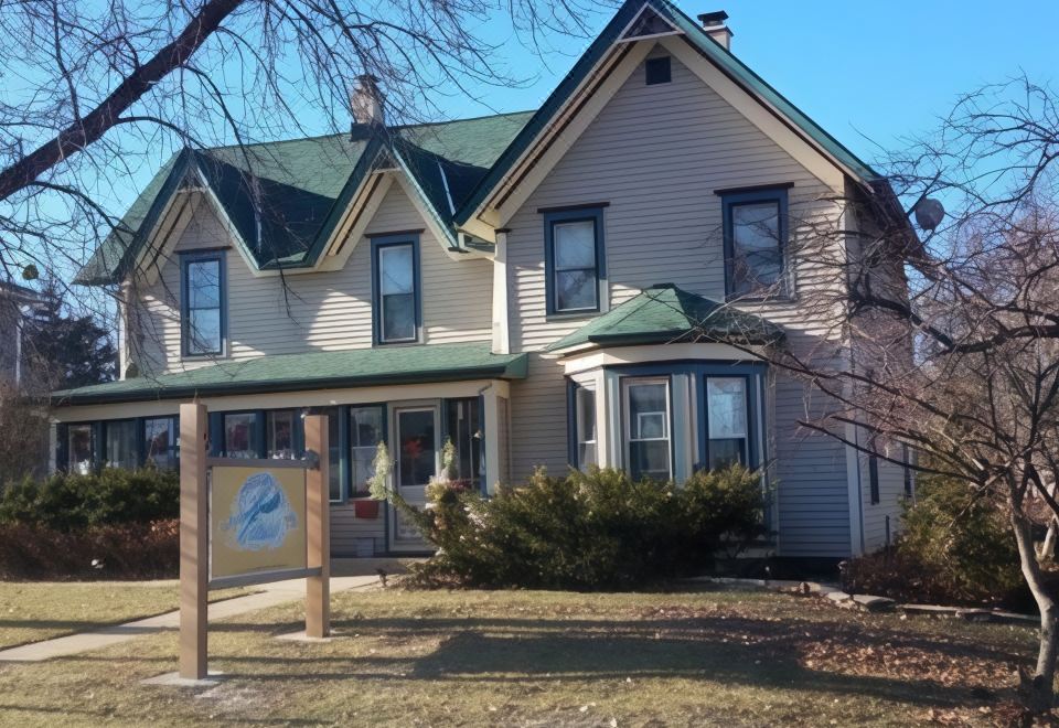 a large two - story house with a green roof , surrounded by trees and grass , and a sign in front of the entrance at Dragonfly Bed and Breakfast