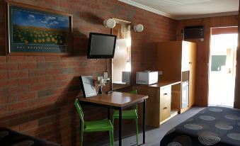 a small room with a brick wall , a table with two chairs , a television , and a microwave at Country Road Motel St Arnaud