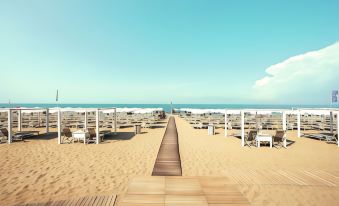 a sandy beach with umbrellas , chairs , and benches lining the boardwalk , providing a pleasant setting for relaxation at Toscana Charme Resort