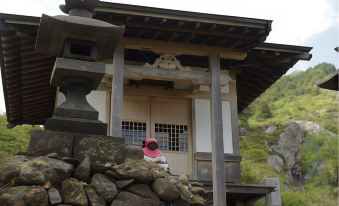 a woman wearing a red jacket is standing in front of a wooden building , possibly a shrine or temple at Manza Kogen Hotel