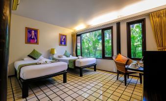 a hotel room with two beds , a chair , and a window overlooking a lush green garden at Baan Amphawa Resort & Spa