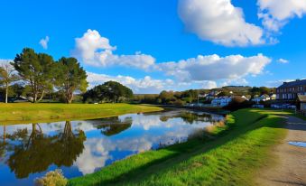 a serene landscape with a river , green grass , and blue skies , under a partly cloudy sky at Hustyns Resort Cornwall