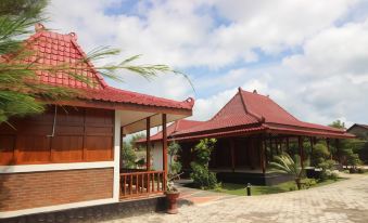 a traditional indonesian building with red roofs and a stone terrace , surrounded by lush greenery at The Royal Joglo