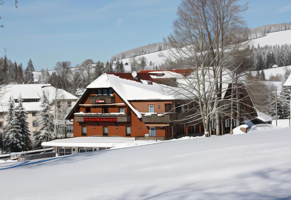 "a large red house with a sign that reads "" lake creek lodge "" is surrounded by snow and trees" at Hotel Faller