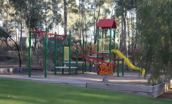 a colorful playground with various play equipment , including slides and swings , situated in a grassy area surrounded by trees at A-Line Holiday Park