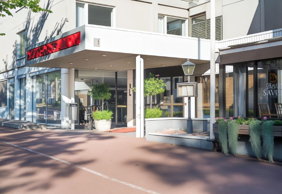 a modern building with a red awning and multiple potted plants in front , under a clear blue sky at Hotel Savoy