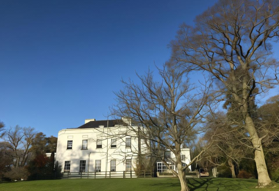 a large white building surrounded by a lush green lawn , with trees and bushes in the background at Leixlip Manor Hotel