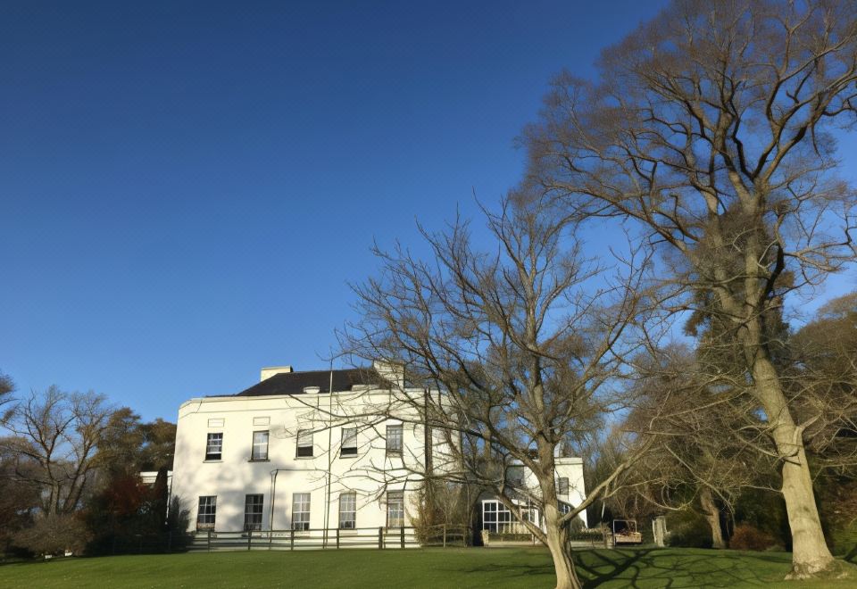 a white house with a white fence and trees in front of it on a sunny day at Leixlip Manor Hotel