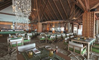 a large dining room with multiple tables and chairs , some of which are covered in green tablecloths at Constance Moofushi