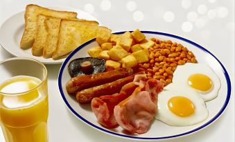 a plate of breakfast food , including eggs , ham , bacon , sausage , and beans , accompanied by toast and orange juice at Days Inn by Wyndham Tewkesbury Strensham