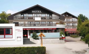 a hotel with a red door and white walls , surrounded by trees and grass , under a clear blue sky at Stern