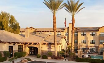 a large building with a flagpole and palm trees in front of it , under a clear blue sky at Residence Inn Phoenix Goodyear
