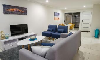 a living room with a gray couch , blue chairs , and a flat screen tv mounted on the wall at Direct Collective - Breeze on Brightwater