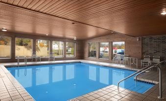 a large swimming pool with a tiled floor and walls is surrounded by windows and has a stationary rail at Days Inn by Wyndham Stoughton WI.