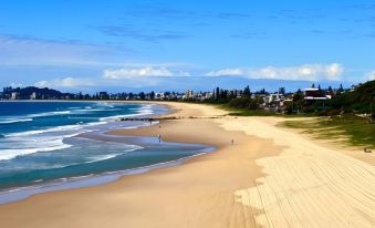 a serene beach scene with clear blue water , sandy shoreline , and a small town in the distance at Sanctuary Beach Resort