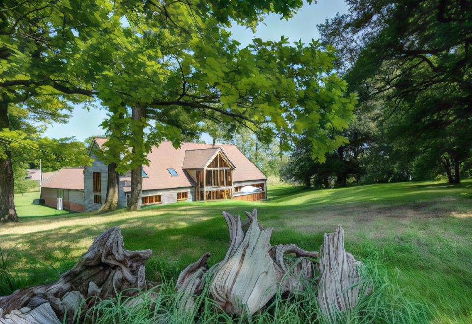 a large house surrounded by trees , with a grassy field in front of it , and a campfire burning in the background at South Park Farm Barn