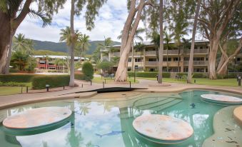 a large outdoor swimming pool surrounded by palm trees , with people enjoying their time in the pool area at Mantra Amphora