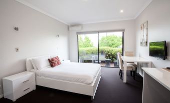 a large white bed is in a room with a table and chairs , and sliding glass doors leading to a balcony at Springwood Motor Inn