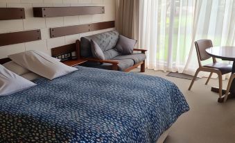 a hotel room with a bed , couch , and table , along with curtains and a window at Toora Lodge Motel