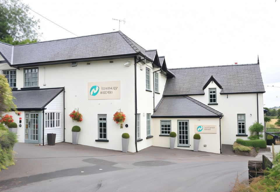 "a white building with a sign that reads "" masters of tattoos "" has two large windows and flower pots on the front" at The Newbridge on Usk