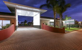 a modern , white building with a red brick entrance and palm trees in front of it at Morphettville Motor Inn