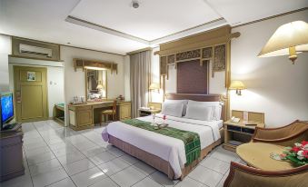 a large bed with white linens and a green throw is in the center of a room with tile flooring at Kusuma Sahid Prince Hotel Solo