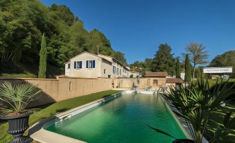 a large swimming pool is surrounded by a stone wall and trees , with a house in the background at Hotel Saint-Martin - Younan Collection