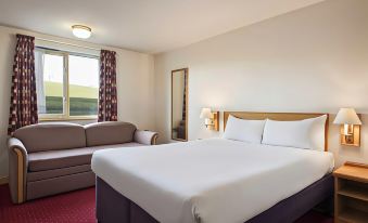 a hotel room with a large bed , a couch , and a window overlooking the city at Days Inn by Wyndham Tewkesbury Strensham