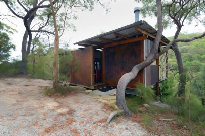 a small wooden house surrounded by trees and bushes , with a porch and a fire pit at Spicers Sangoma Retreat