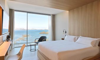 a modern hotel room with a large window overlooking the ocean , featuring a white bed and wooden furniture at Noa Boutique Hotel