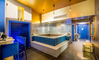 a large , blue bathtub is in the center of a room with tile flooring and a gray wall at Arthouse Hotel