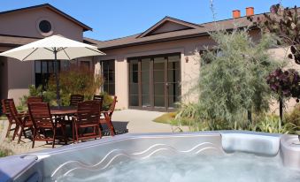 a patio area with a hot tub , dining table , chairs , and an umbrella , surrounded by a lush green garden at The Summit Lodge