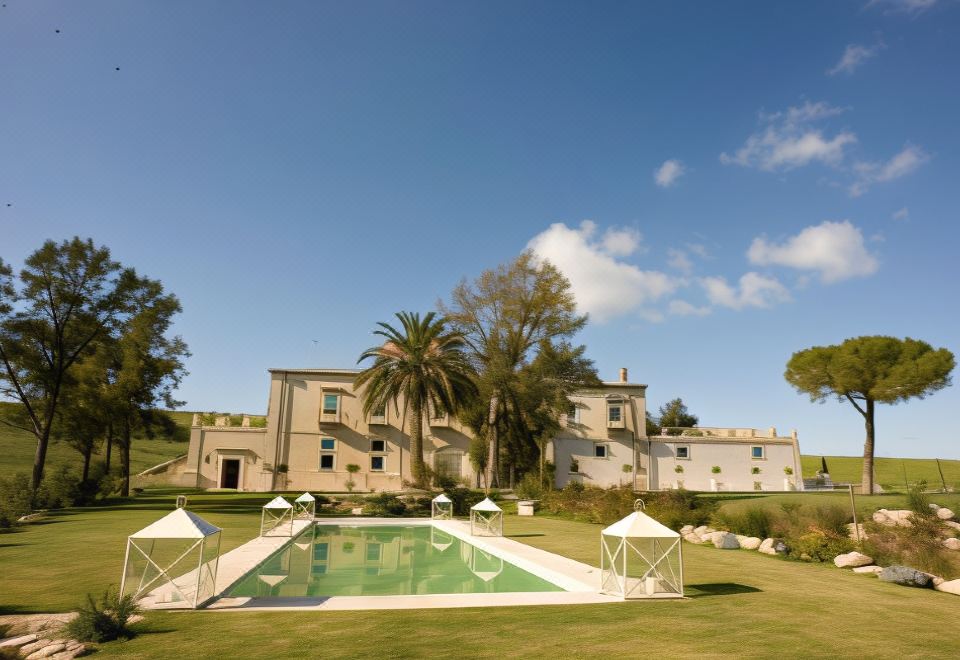 a large white building with a pool and lounge chairs in front of it , surrounded by green grass and palm trees at Castello Camemi