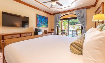 a large bed with a white comforter is in a room with a television and sliding glass doors at Coco Beach Resort