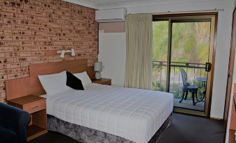 a hotel room with a white bed , brick wall , and a sliding glass door leading to a balcony at Bridge View Motel