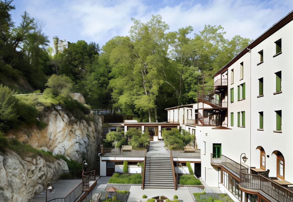 a modern , white building with green balconies and stone walls , surrounded by lush greenery and stone paths at Le Grand Hotel