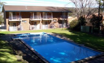 an outdoor swimming pool surrounded by a grassy area , with a building in the background at Waterview Gosford Motor Inn