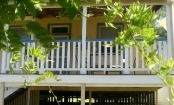 a white balcony with blue railings , surrounded by green trees and plants , under a clear blue sky at Cypress Ridge Cottages