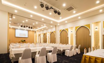 a large conference room with white tables and chairs , and a stage at the front at Alfahad Hotel