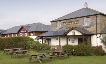 a brick building with a wooden roof , situated next to a grassy area and a body of water at Premier Inn Newquay (Quintrell Downs)