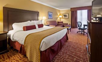 a large bed with a red blanket and gold throw is in the middle of a room at Best Western Plus Wilkes Barre Center City